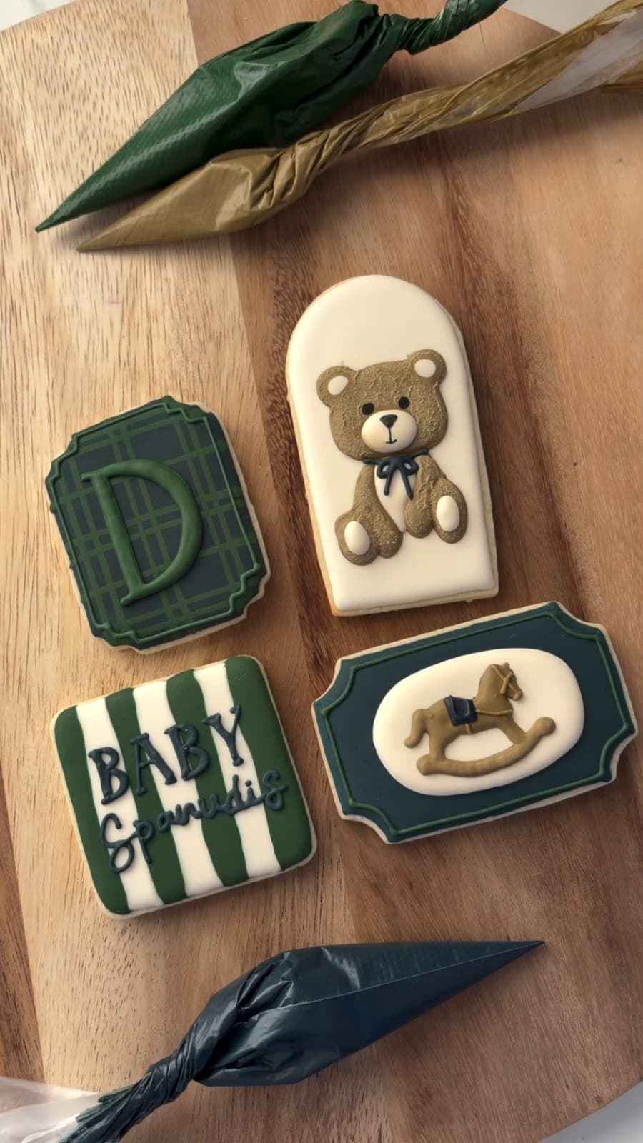 Green and navy baby shower cookies with a teddy, a plaid letter, and a rocking horse